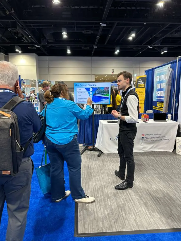 A member of the Atlantic Media Company team walking two attendees through the Our Proven Pipeline slide at the booth